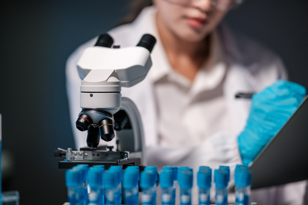 Asian female scientist looking under microscope, analyzes petri dish sample. specialists working on medicine, biotechnology research in advanced pharmacy lab, Medical development laboratory.